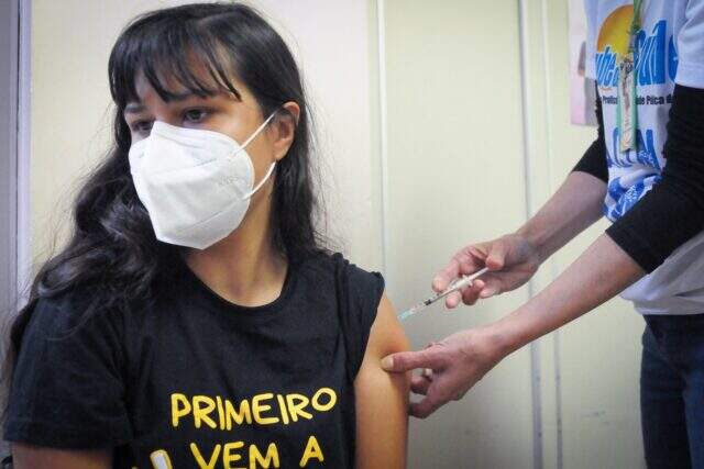 adolescente com camiseta preta sendo vacinada no braço